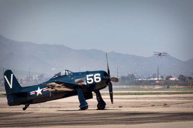 Arizona, Tucson 'daki 2023 Thunder and Lightning Over Arizona hava gösterisinde çift kanatlı bir uçak sahnedeyken bir F-8F Bearcat pistte oturuyor..