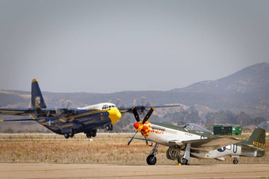 Minik Willy II adlı bir P-51 Mustang pistte otururken, ABD Donanması Mavi Melekleri C-130 destek uçağı Şişko Albert, Miramar, Kaliforniya 'daki Amerika' nın 2023 sayılı Airshow 'unda havalanıyor..