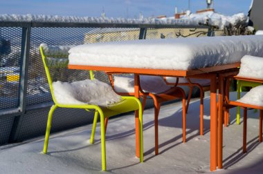 Kar kaplı metal mobilyalar, karla kaplı masa ve terasta sandalyeler.