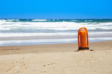 Lifeguard rescue can on the beach. Orange rescue buoy in vertical position on the sand. Photo image with copy space.