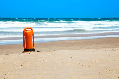 Lifeguard rescue can on the beach. Orange rescue buoy in vertical position on the sand. Photo image with copy space.