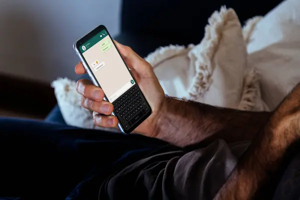 Ekranda sohbet uygulaması olan bir adam elinde cep telefonuyla kanepede dinleniyor. Akıllı telefonuyla mesaj gönderiyor..