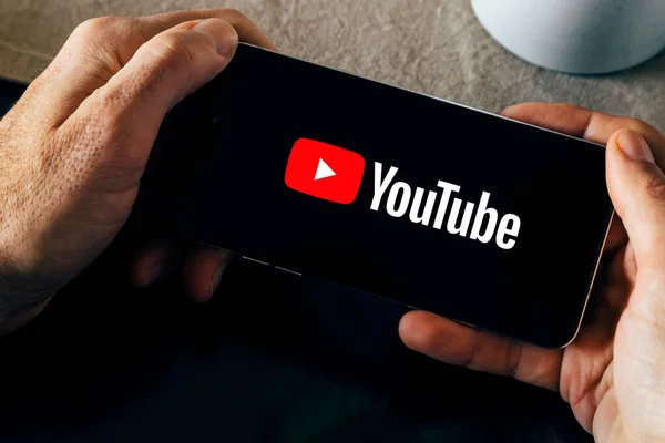 Akıllı telefon ekranında YouTube logosu. Uygulama açıkken akıllı telefon tutan bir adam. Cep telefonundaki video yayını uygulaması. Rosario, Arjantin - 23 Kasım 2023