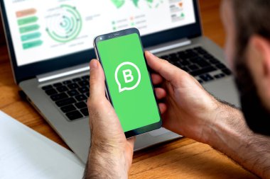Whatsapp Business uygulamasının logosu cep telefonunun ekranında bir adamın elinde. Yeşil arka plan ekran ve beyaz logolu akıllı telefon. ROSARIO, ARJANTINA 1 ARALIK, 2023