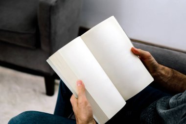 Kitap okuyan bir adam. Boş sayfa kitaplarının maketi için ideal fotoğraf. Oturma odasında oturan adam elinde açık bir kitap tutuyor..
