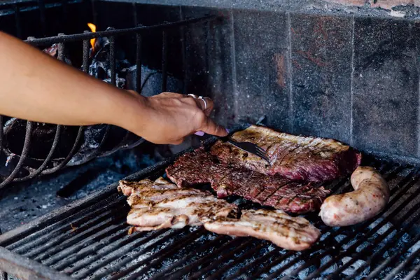 Woman making a barbecue. He is prodding the meat with a fork.