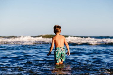 Denizde yıkanan çocuk. Güneşli bir yaz günü, gün batımında okyanus dalgalarında eğlenen bir çocuk. Çocuk dışarıda eğleniyor..