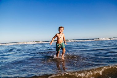 Güneşli bir yaz günü, gün batımında okyanus dalgalarında eğlenen bir çocuk. Çocuk dışarıda eğleniyor..