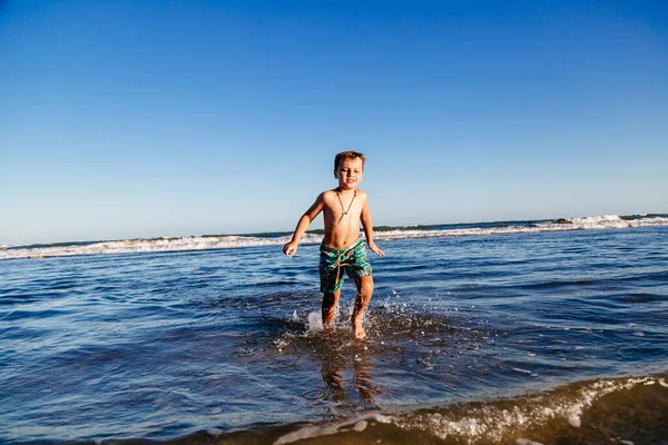 Güneşli bir yaz günü, gün batımında okyanus dalgalarında eğlenen bir çocuk. Çocuk dışarıda eğleniyor..