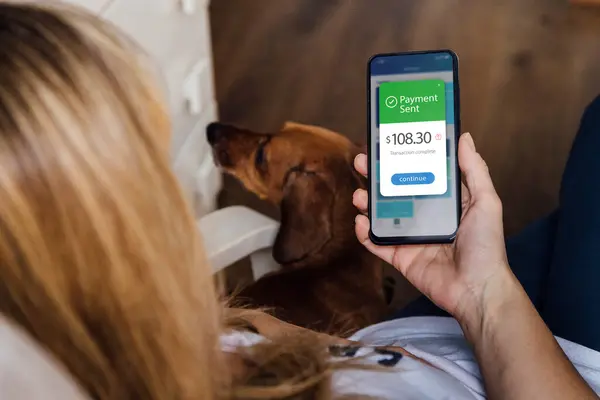 Mobile phone with a financial application on screen. Relax woman with her dog, transfers money online using applications to send and receive currency. Money transfer concept.