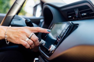 Kadının eli arabasındaki dokunmatik ekrana bastırıyor. Araba bilgisayarı ekranından bir uygulama seçer.