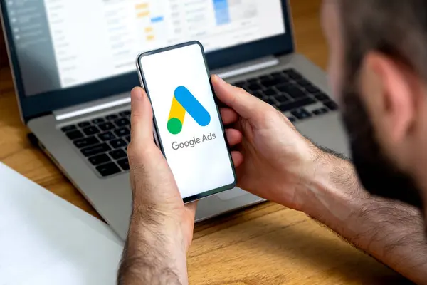 Ekranda Google reklamları olan bir cep telefonu kullanan bir adam ve arka planda reklam istatistiklerini gösteren bir bilgisayar. San Francisco, Kaliforniya, ABD - 23 Mayıs 2024.