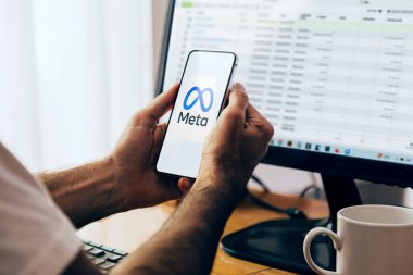 Cep telefonu ekranında Meta logosunu gösteren bir akıllı telefon tutan adam. Arka planda monitörde Facebook İş Yöneticisi olan bilgisayar. Rosario, Arjantin - 20 Haziran 2024.