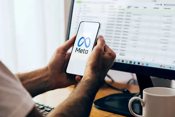 Cep telefonu ekranında Meta logosunu gösteren bir akıllı telefon tutan adam. Arka planda monitörde Facebook İş Yöneticisi olan bilgisayar. Rosario, Arjantin - 20 Haziran 2024.