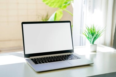 Laptop beyaz ekranlı bir masanın üzerinde. Olay yerinde hiç insan yok. Bilgisayar pencerenin yanında. Net, parlak renklerde stok fotoğrafları.