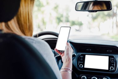Kadın sürücü cep telefonu ve arabanın dijital kontrol ekranı ile etkileşime geçiyor. Model için akıllı telefon ve araba bilgisayar ekranının boş görüntüsü.