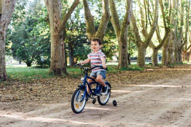 Parkta bisiklet süren gülümseyen küçük çocuk..