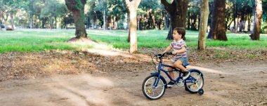 Parkta bisiklet süren gülümseyen küçük çocuk. Yatay web pankartı biçimi.