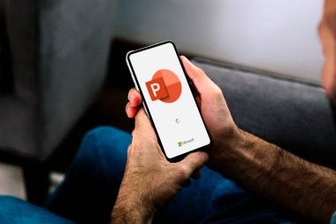 Microsoft Office PowerPoint 'in logosunu ekranda gösteren cep telefonu kullanan bir adam. Güç noktası bir sunum programıdır. ROSARIO, ARJANTINA - 5 Nisan 2025.