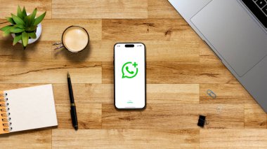 Iphone ekranında Whatsapp 'ın yeni logosu. Çalışma alanının en üst görüntüsü. Bilgisayarlı masa masası, cep telefonu, kahve, not defteri, kalem ve bitki. Rosario, Arjantin - 10 Haziran 2025