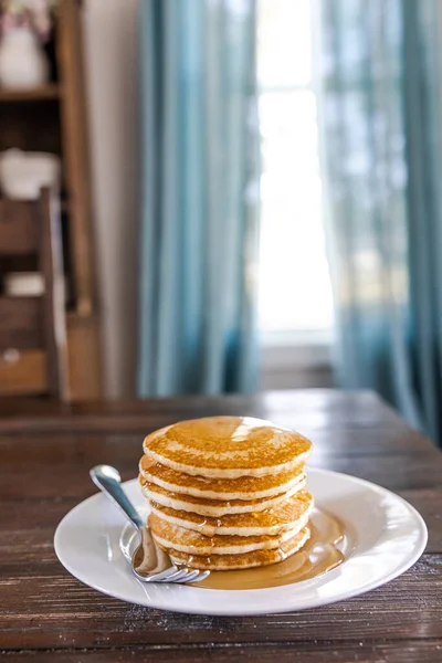 A plate with a stack of plain homemade pancakes at a dark wood kitchen dining room table.