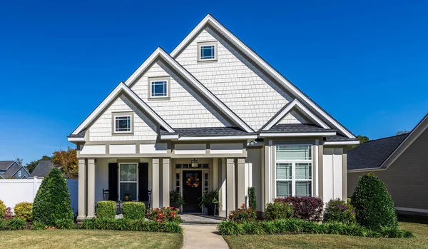The front view of a new construction cottage craftsman style white house with a triple pitched roof with a sidewalk, landscaping and curb appeal.