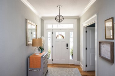 An open large and wide interior front door hallway foyer with transom, hanging light fixture, coastal colors and entry way table and wood floors. clipart