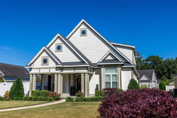The front view of a new construction cottage craftsman style white house with a triple pitched roof with a sidewalk, landscaping and curb appeal.