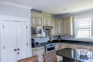 A cream colored new construction kitchen with black granite countertops and wood flooring and stainless steel appliances.