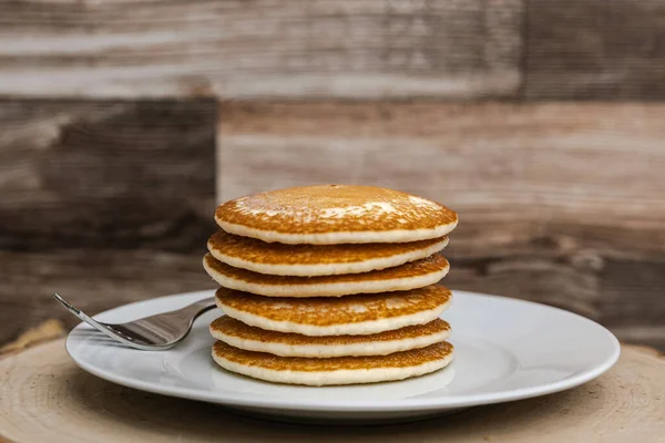 A large plate stack of pancakes with a fork against a wood background plain with no syrup.