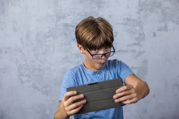 A little caucadian boy with glasses playing with his electronics tablet for screen time with copy space.