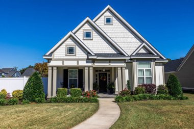 Front view of a new construction cottage craftsman style white house with a triple pitched roof with a sidewalk, landscaping and curb appeal.