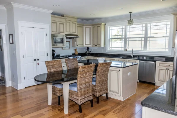 A cream colored new construction kitchen with black granite countertops and wood flooring and stainless steel appliances and an eat-in dining area.