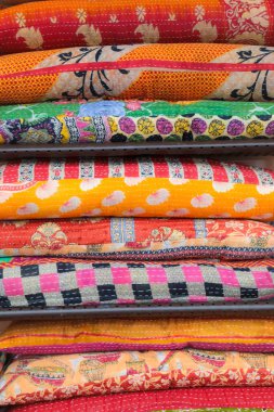 Colorful blankets and quilts placed in a stack in bright and vibrant orange and red colors.
