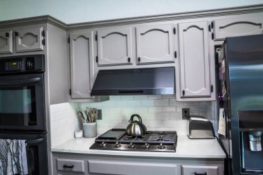 Eski bir evde yenilenmiş bir mutfak, gri dolaplar, mermer tezgahlar, küçük taşınabilir bir ada ve fayanslı bir zemin..