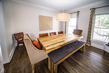 Lekeli ahşap bir masası olan modern bir yemek odası, bankta oturan ve davul lambası armatürüne sahip döşenmiş sandalyeler..