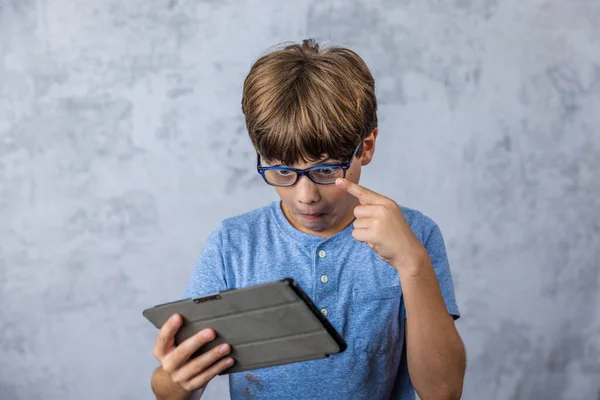 A little caucadian boy with glasses playing with his electronics tablet for screen time with copy space.