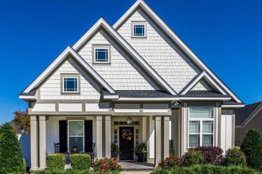 The front view of a new construction cottage craftsman style white house with a triple pitched roof with a sidewalk, landscaping and curb appeal.