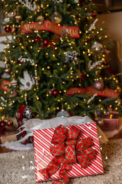 stock image Christmas tree with lights and ornaments and a beautifully wrapped present underneath with a large bow.