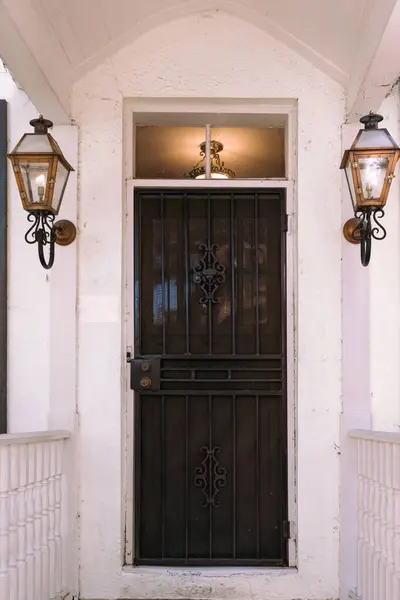 A dark stained wood door on a cream colored old house with flanked gas lanterns.