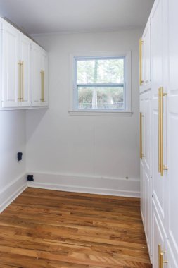 Yeni yenilenmiş, ahşap döşemeleri olan boş bir çamaşır odasında zarif altın ve ince donanımlı beyaz titreşimli dolaplar..