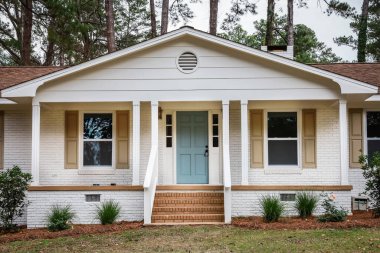 The front exterior entrance of a newly painted white siding brick ranch style house with a large yard that has been recently renovated. clipart