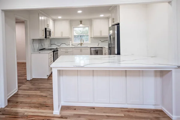 A light and bright newly remodeled white kitchen with quartz countertops, white shaker cabinets and gold hardware and stainless appliances and a large island.