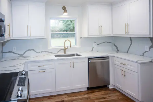 A light and bright newly remodeled white kitchen with quartz countertops, white shaker cabinets and gold hardware and stainless appliances.
