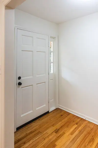 The empty entrance of a newly renovated and painted white house with hardwood floors and a wide front door.
