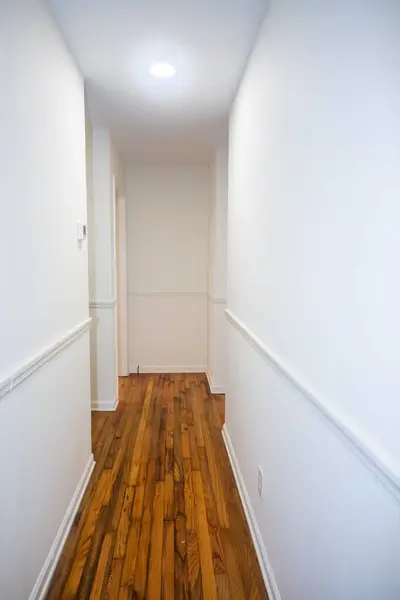 An empty white hallway in a house with stained hardwood floors.
