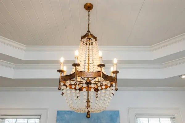 An ornate beaded chandelier light fixture with glowing lit candle type bulbs against a double tray white ceiling.