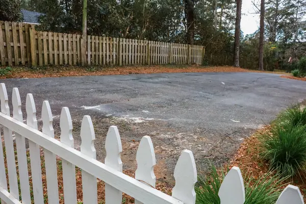 Short white picket fence surrounding a backyard to the paved driveway.