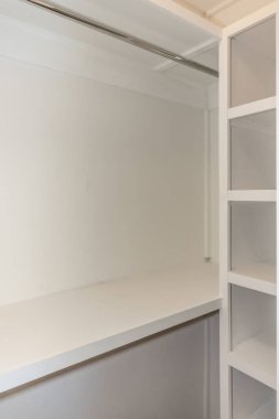 Ahşap rafları ve eski bir evde giysi barı olan içi beyaz, katı ahşap bir dolap..
