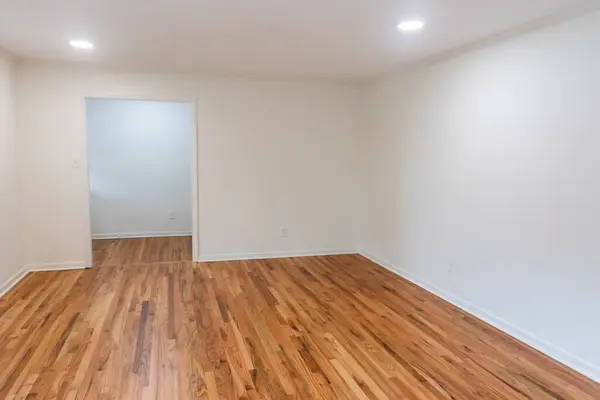 A house for sale with an empty white living room or den of a newly renovated and painted house with dark hardwood floors.